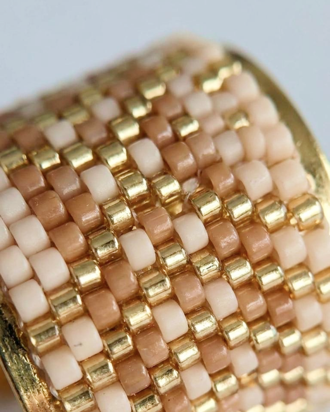 Macro detail of a handwoven Miyuki ring in nude, beige, and gold tones.