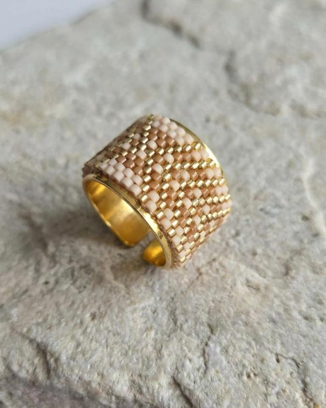Adjustable nude and gold Miyuki ring displayed on a stone surface.