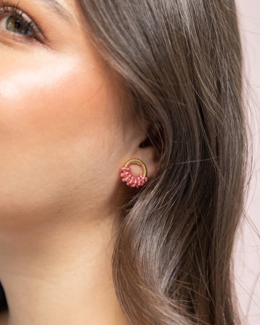 Side-profile model wearing gold mini-ring stud earrings with a cluster of pink beads.