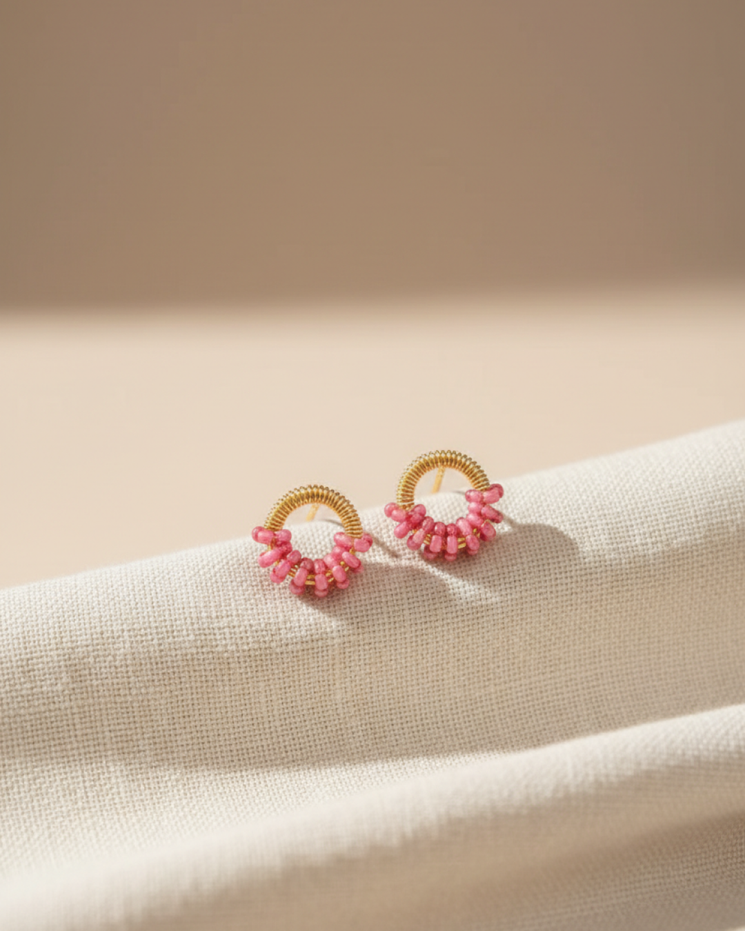 Pair of gold textured mini-ring stud earrings with pink murano-style clusters on a neutral backdrop.