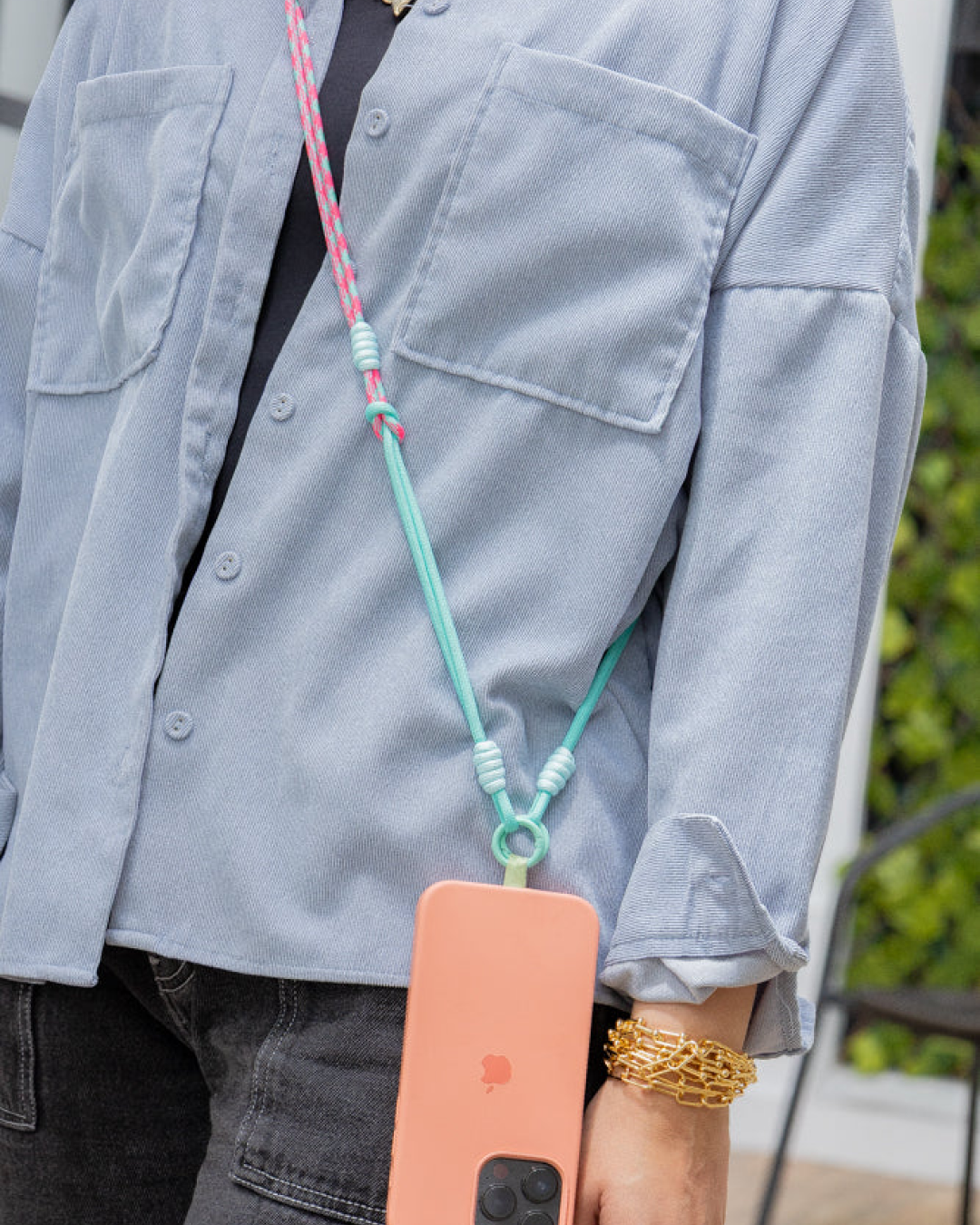 Model wearing a mint and pink phone strap with a coral phone case.