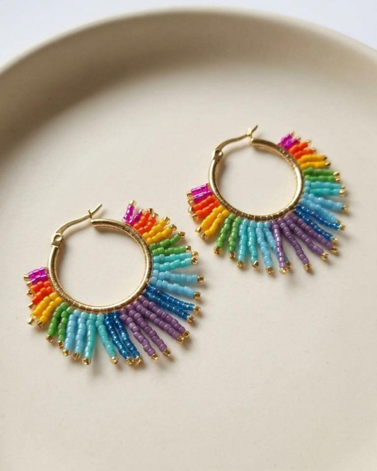 Pair of gold hoop earrings with rainbow-effect Miyuki fringe displayed on a white tray.