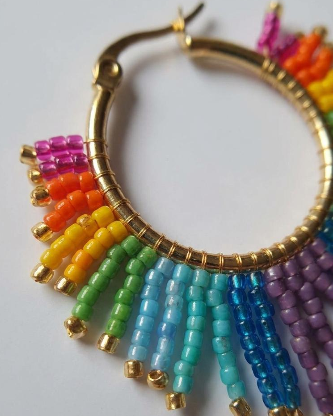 Macro detail of a rainbow hoop earring with vibrant Miyuki beads.