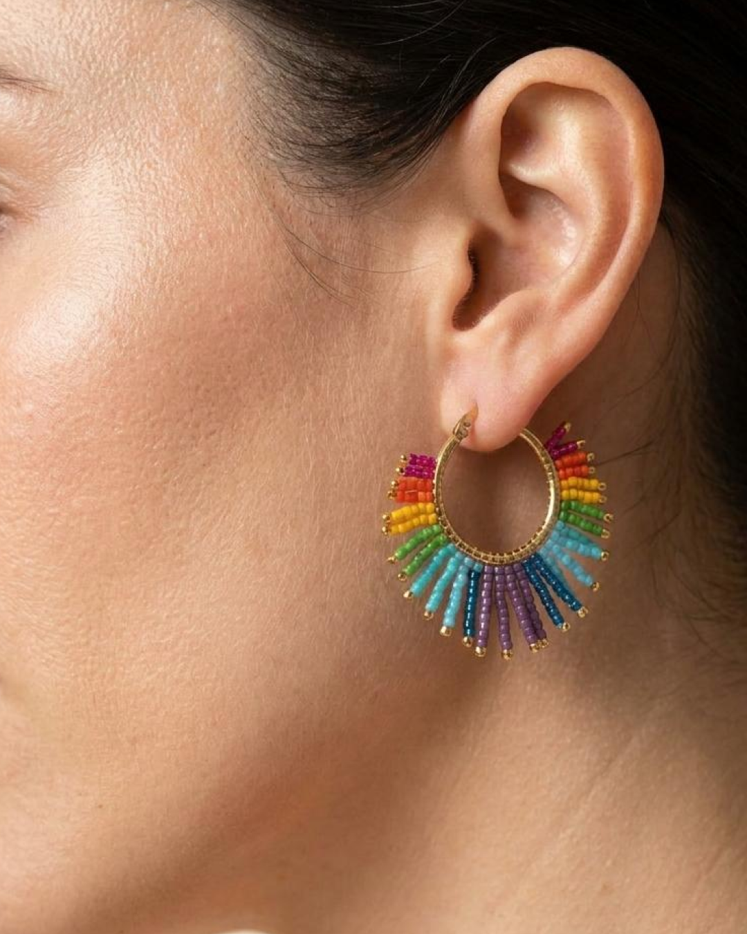 Woman wearing a gold hoop earring with multicolor Miyuki fringe.