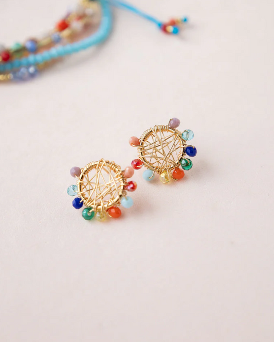 Pair of gold circular studs with rainbow Murano beads on a light surface, bracelet blurred in the background