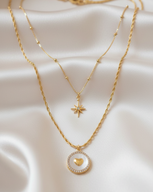 Layered gold necklace set: star pendant and circular heart medallion on light satin fabric.