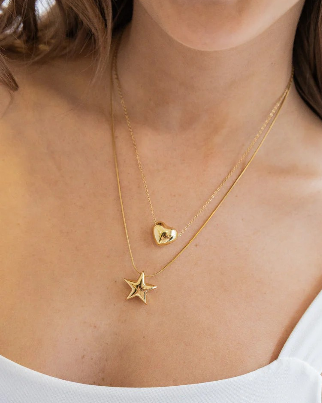 Layered gold double necklace with heart and star pendants on model’s neckline.