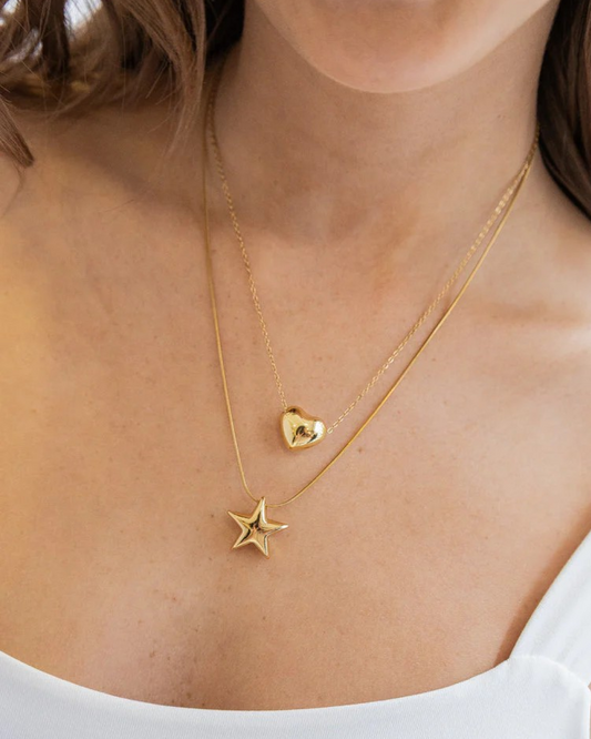 Layered gold double necklace with heart and star pendants on model’s neckline.