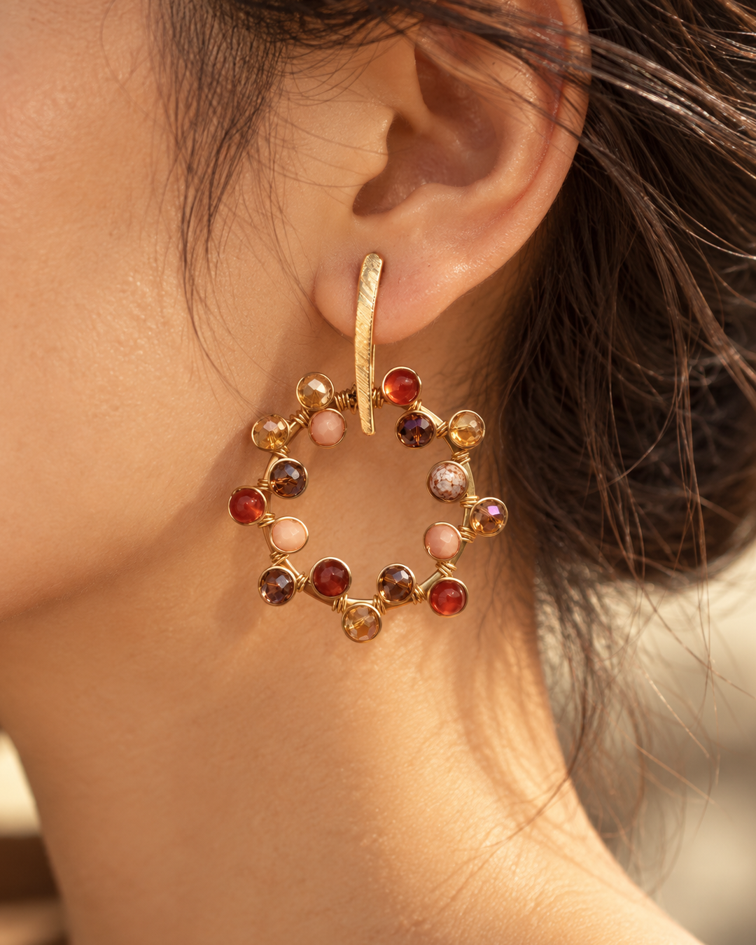 Close-up of a gold-plated circular drop earring featuring amber, brown, red, and pink beads worn on the ear.