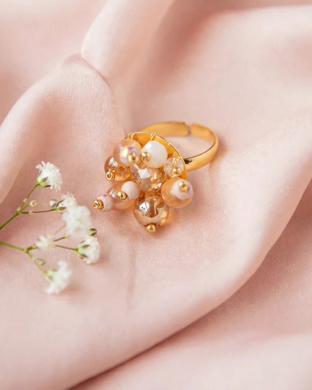 Nude Bouquet adjustable ring with 24K gold-plated brass band and a cluster of champagne, ivory, and blush glass beads, displayed on soft pink satin.
