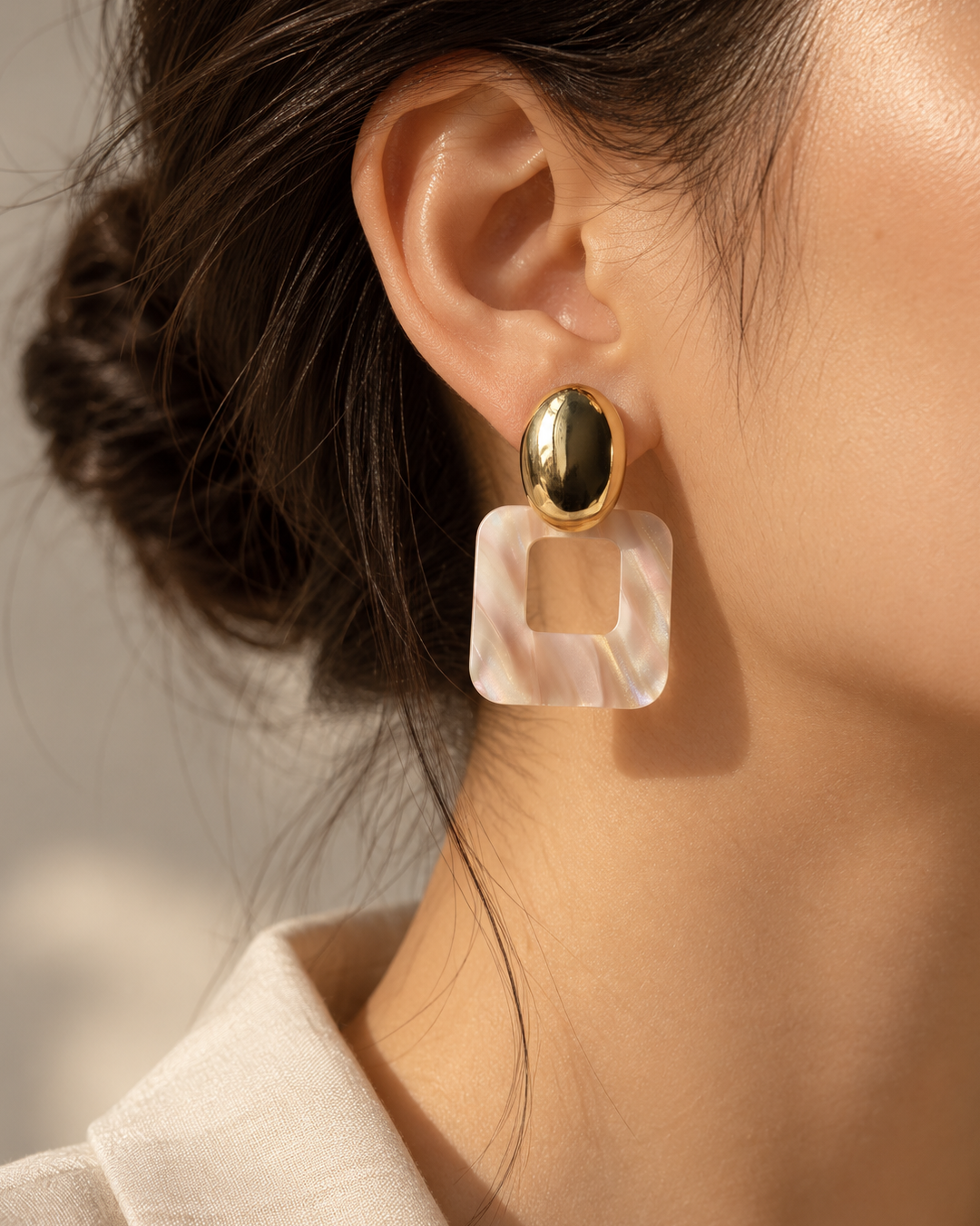 Woman wearing Rosé Frame earrings with gold oval studs and pearlescent pink geometric resin drops, styled with a neutral outfit.