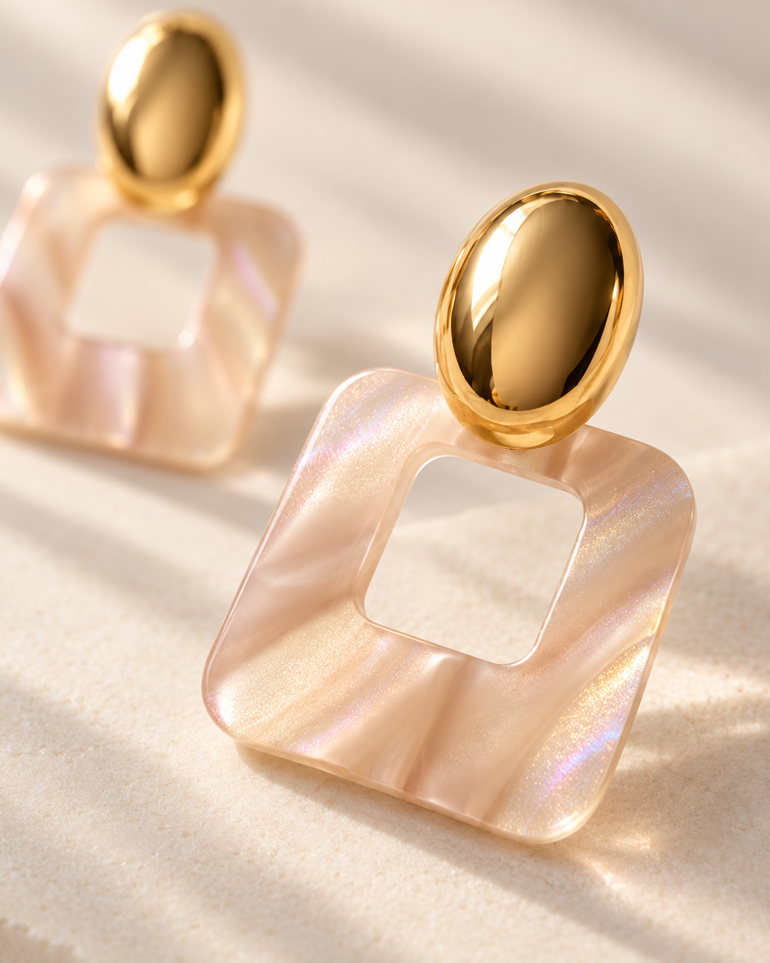 Rosé Frame drop earrings featuring polished gold oval studs and iridescent blush pink square resin pendants with open centers.